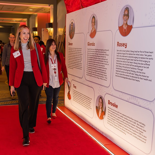 Woman in red jacket walking down hallway lined with survivor photos and stories.